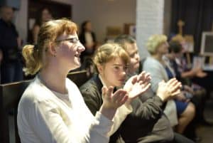 Ludzie siedzą na widowni. Klaszczą w ręce.