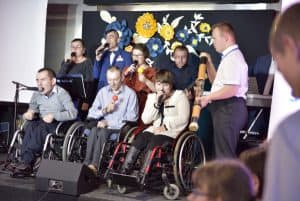 Ludzie na wózkach inwalidzkich są na scenie. Niektórzy trzymają grzechotki inni bębenki.