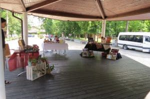 Stoły nakrte stoją w zadaszonej altanie. W tle drzewa i bus.