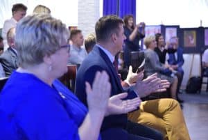 Ludzie siedzą na scenie. Klaszczą w dłonie.