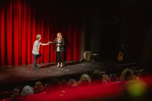 Dwie osoby na scenie - kobieta i mężczyzna trzymają się za ręce.