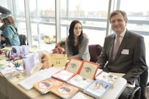 Mężczyzna z kobieta siedzą przy stole z kartkami robionymi ręcznie. Uśmiechają się o zdjęcia.