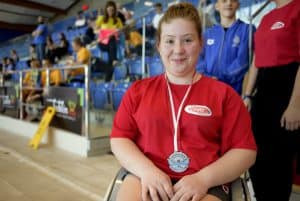 Dziewczyna pozuje do zdjęcia z medalem. Jest uśmiechnięta.