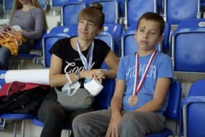 Chłopczyk i kobieta siedzą na trybunach. Chłopiec ma na sobie medal.