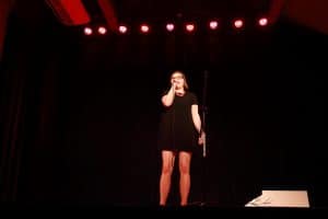 Na scenie stoi dziewczyna. Ma mikrofon blisko twarzy.