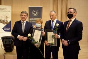 Cztery osoby pozują do zdjęcia. Kobieta i mężczyzna w środku trzymają dyplom i róże.