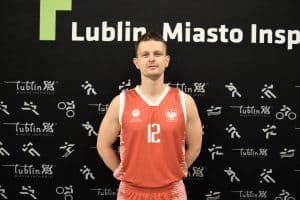 Sportowiec w czerwonej koszulce pozuje do zdjęcia na tle czarnej ścianki z napisem Lublin Miasto Inspiracji.