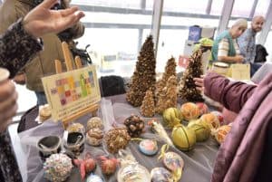 Stół zastawiony rękodziełami. W tle starsi ludzie siedzący przy stole.