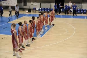 Sportowcy stoją w jednym rzędzie na boisku. Mają na sobie czerwone ubrania.