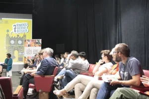 Grupa osób siedzi na fotelach i słucha wystąpienia. Są ustawieni bokiem do obiektywu.