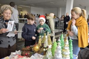 Ludzie stoją nad stołem zastawionym rękodziełami. JEdna z kobiet trzyma kartkę w dłoni.