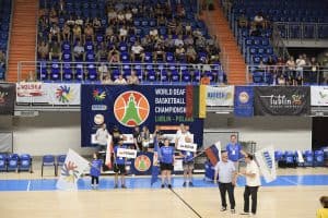 Na widowni siedzą osoby. Poniżej na boisku stoją osoby i trzymają flagę Polski i Rosji. Po prawej stronie stoi dwóch mężczyzn.