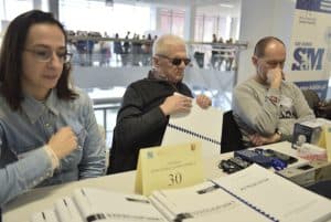 Ludzie siedzą przy stole z broszurami. Ich twarze są zamyślone.