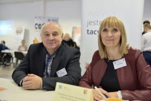 Kobieta z mężczyzną siedzą przy stole. Uśmiechaja sie do zdjęcia.