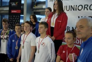 Chłopcy i dziewczyny pozują do zdjęcia w medalach. Po prawej stronie stoi starszy mężczyzna.