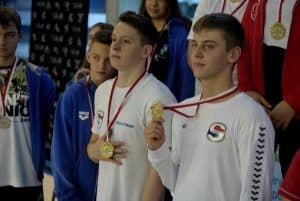 Chłopcy stoją i pokazują medale. Jeden z nich trzyma medal w ręce.