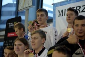 Chłopaki pozują do zdjęcia. Pokazują medale i są uśmiechnięci.