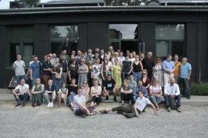 Grupa osób pozuje do fotografii przed budynkiem. Jest ich kilkanaścioro.