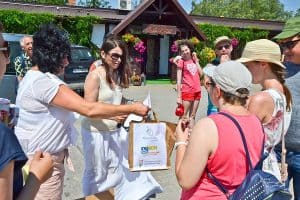 Na pierwszym planie znajdują się cztery kobiety, są odwrócone do siebie twarzami. Jedna z kobiet po lewej podaje torbę kobietom po prawej, napisane jest na niej „PSCN, Państwowy Fundusz Rehabilitacji Osób Niepełnosprawnych”. W tle znajdują się inne osoby i budynek z napisem „Zacisze”.