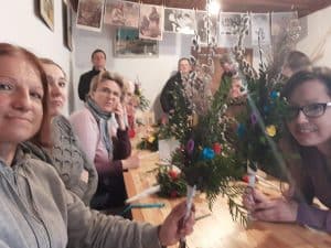 Grupa osób pozuje do zdjęcia. Osoby siedzą przy stole a w rękach mają wykonane palmy. Niektóre osoby patrzą wprost w obiektyw.