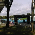 Widok na stadion olimpijski. Między drzewami jest łuk przez który można wejść na tor.