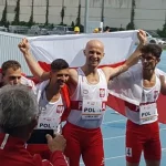 Zawodnicy z Polski pozują do fotografii. Pięciu mężczyzn trzyma Polską flagę.