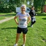 Uczestniczka w stroju sportowym w koszulce z napisem Lublin Business Run 2017 oraz z przypiętym numerem startowym 5545/1 pozuje z uśmiechem do zdjęcia. W tle mężczyzna w stroju sportowym.