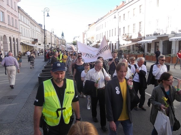 Grupa osób jest na ulicy. Trzymają oni transparent “#STOPPSYCHOFOBII”. Po lewej stronie jest policjant.