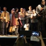 Po prawej Łukasz Jemioła gra na gitarze i śpiewa do mikrofonu, w tle tłum uczestników.