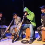 Grupa D-tonacja - trzej chłopcy i mężczyzna pośrodku grają na aborygeńskim instrumencie didgeridoo
