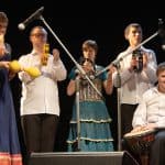 Grupa Bebnloduy - niepełnosprawni muzycy stoją i grają na tamburynach. Po prawej siedzi niepełnosprawny muzyk grający na bębnie.