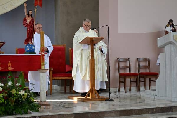 Na ambonie w kościele stoi ksiądz. Ma on mikrofon blisko ust.