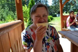 Starsza kobieta pozuje do obiektywu z waflem cukrowym siedząc w altance. Jest uśmiechnięta.