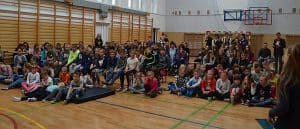 Duża grupa dzieci siedzi na sali gimnastycznej. niektórzy siedzą na materacu.