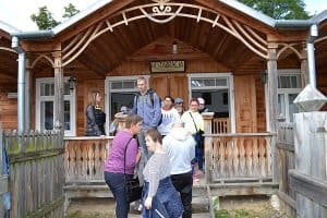 Grupa osób stoi przed drewnianym budynkiem z altanką.