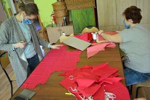 Dwie kobiety siedzą przy maszynach do szycia i pracują.