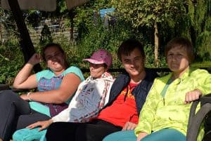 Osoby siedzą na ławce. Jest ich czwórka- trzy kobiety i mężczyzna. Troje z nich patrzy w obiektyw.