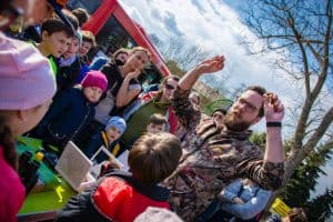 Mężczyzna w okularach otoczony dziećmi pokazuje w dłoniach wnętrze owocu orzecha włoskiego