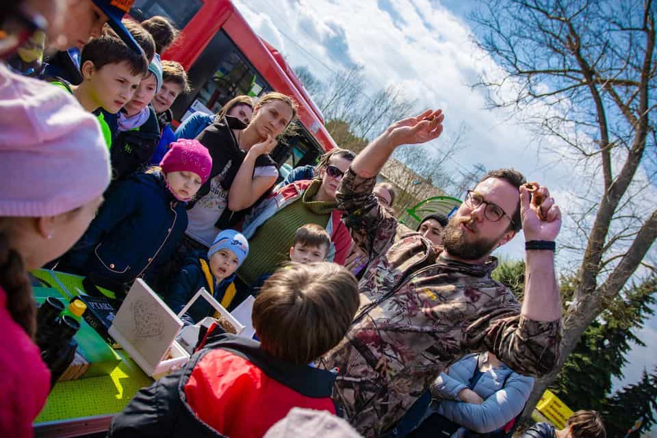 Mężczyzna w okularach otoczony dziećmi pokazuje w dłoniach wnętrze owocu orzecha włoskiego