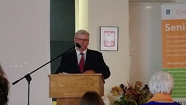 Mężczyzna w garniturze stoi na mównicy i ma przed sobą mikrofon.