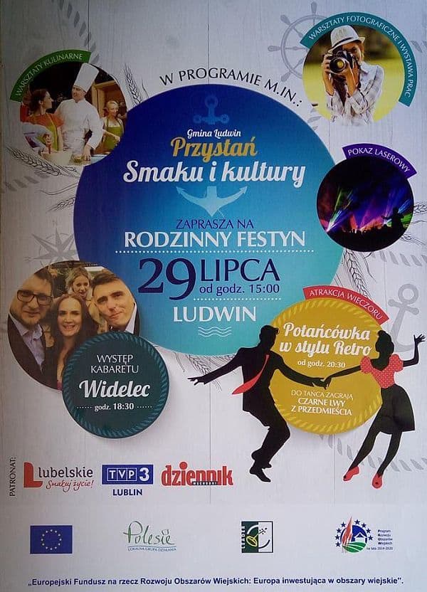 Kobieta stojąca przy stole z rękodziełami pod namiotem w plenerze. Po lewej stronie stoi baner reklamowy z informacją o Polskim Stowarzyszeniu na rzecz Osób z Niepełnosprawnością intelektualną.