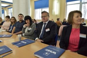 Cztery kobiety i dwóch mężczyzn siedzących przy stole. Niektórzy z nich mają przypięte do ubrań plakietki identyfikacyjne. Na stole teczki z logiem WSEI.