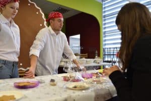 mężczyzna wraz z kobietą stoją przy stole na którym są ciasteczka. Na głowach mają czerwone arafatki.