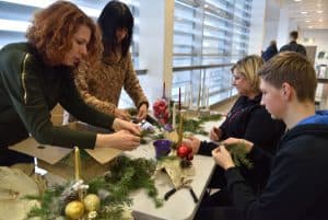 Dwie kobiety przy stole zastawionym ozdobami i rękodziełami świątecznymi. Na sole stroiki świąteczne ze świecami.