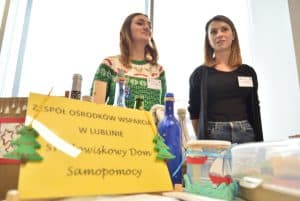 Dwie młode kobiety stojące za stołem z rękodziełami. Jedna z nich uśmiecha się.