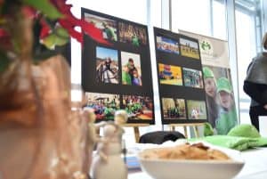 Sztalugi na których są kolaże ze zdjęć. Obok sztalug stół na którym są położone zielone koszulki i zielona czapka z daszkiem.