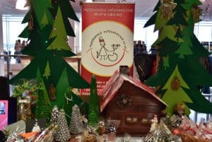 Stół zastawiony pracami manualnymi. Są duże choinki ręcznie wycinane, chatka oraz mniejsze figurki choinek świątecznych.