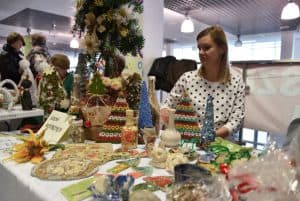 Kobieta siedząca przy stole z rękodziełami. Na stole różne choinki, wazony zdobione techniką decoupage.