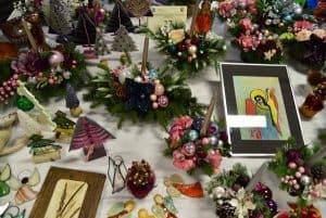 Na stole ręcznie robione stroiki świąteczne ze świeczkami i gałązkami iglaków. Na stole także malowane obrazy aniołów.