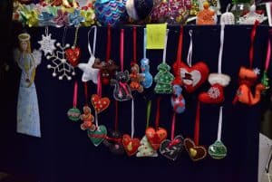 Figurki materiałowe przewieszone są przez stół. Są świąteczne skarpety, choinki, aniołki, ciasteczkowe ludziki, kotki, śnieżynki.